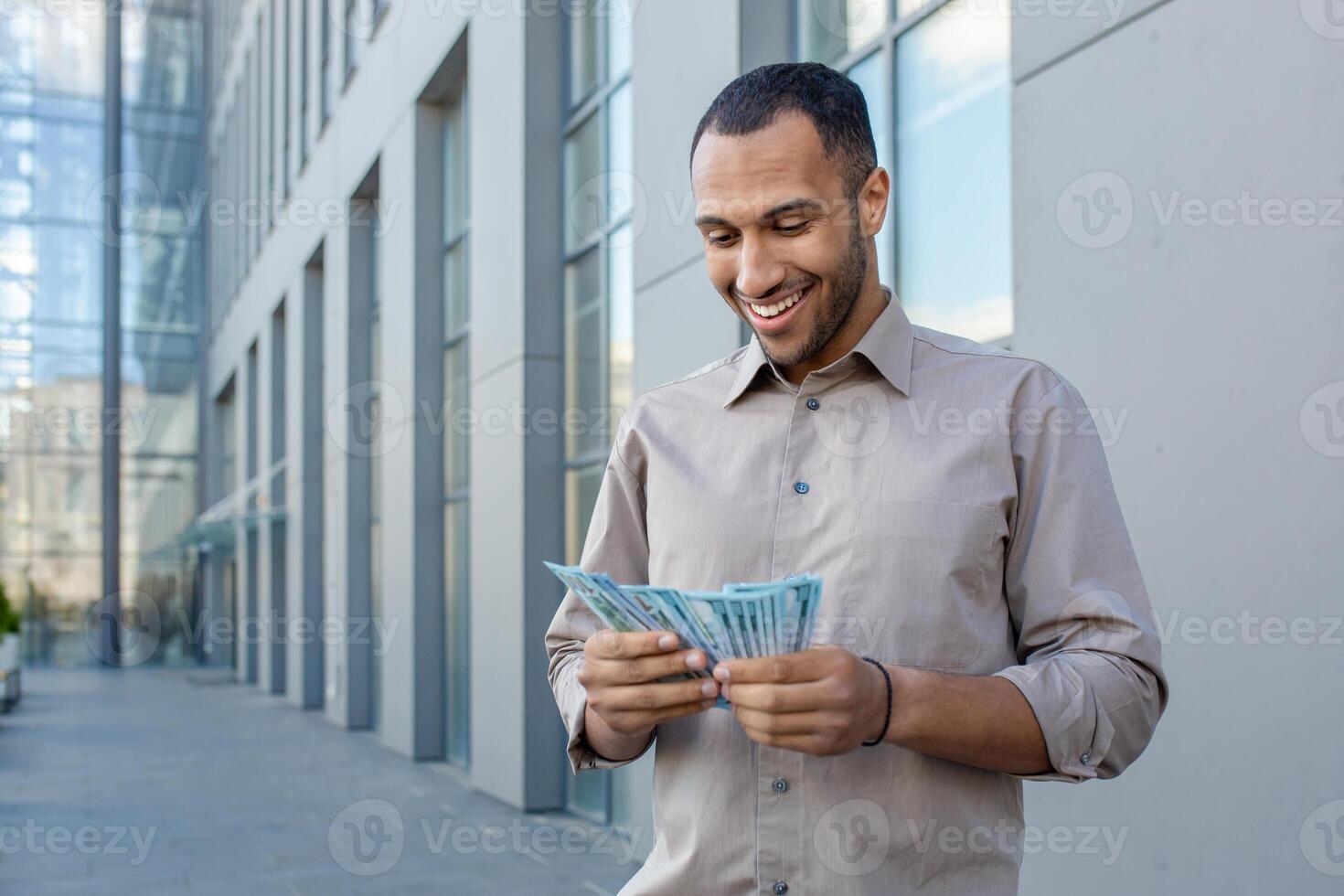 Smiling man counting money outdoors near modern office building, expressing financial success and prosperity photo
