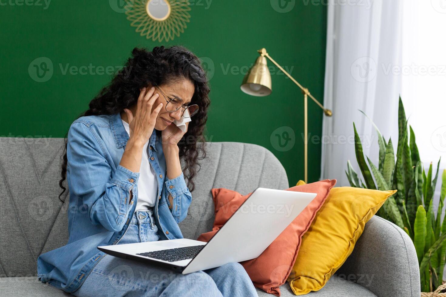 Online consultation with a psychologist, a psychotherapist, a crying woman sitting on a sofa in a living room with a laptop, talking remotely with a doctor, using a call. photo