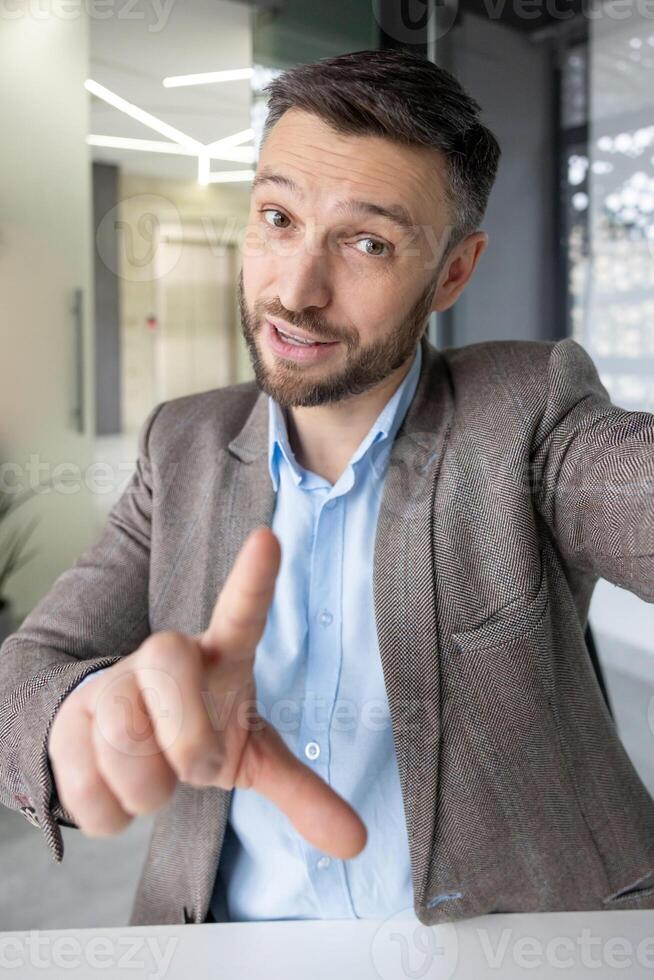 A professional middle-aged man participates in a call, gesturing while conversing. He is in a stylish, contemporary office setting, wearing a suit and a friendly expression. photo