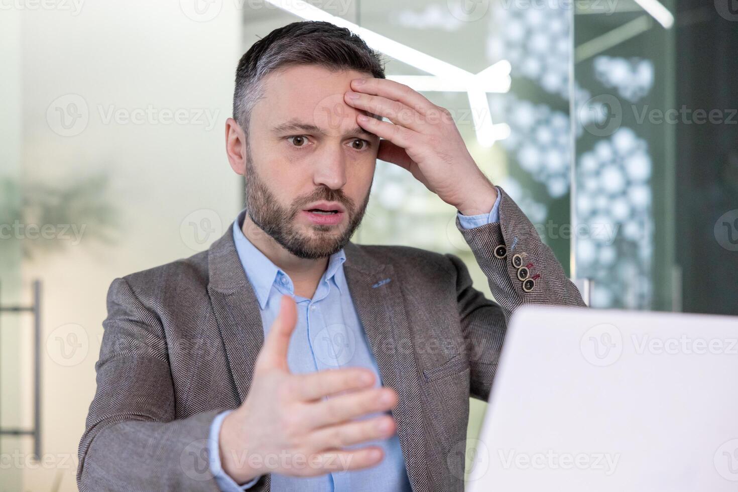 A professional businessman appears confused and stressed while working at his laptop in a modern office environment. photo