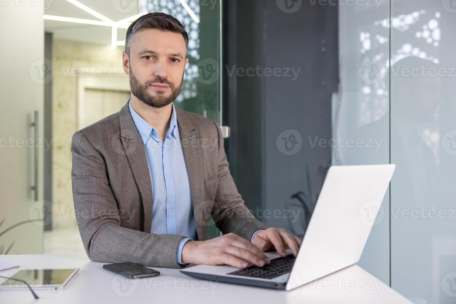 A focused professional man in a suit working intently on a laptop in a modern office setting, exuding a serious demeanor. photo
