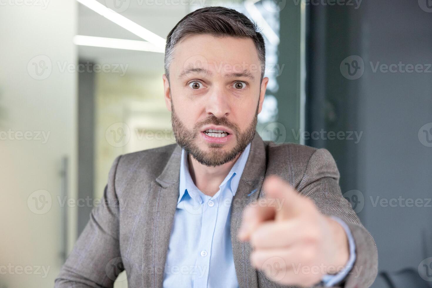 An irate businessman pointing a finger while talking angrily on a call, showing frustration and aggression. photo