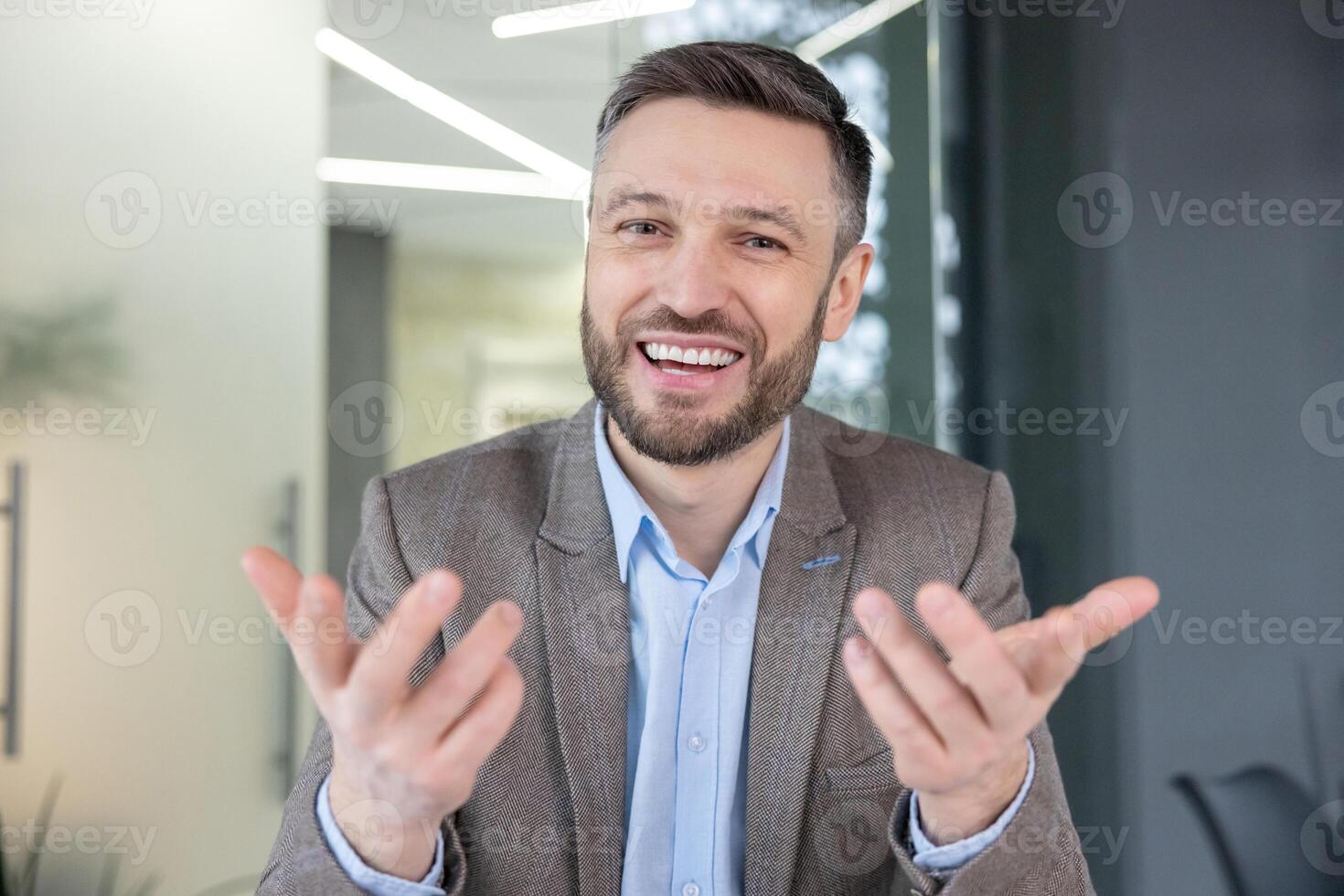 Smiling professional man in a suit offering a friendly gesture in a bright contemporary office setting, exuding confidence and approachability. photo