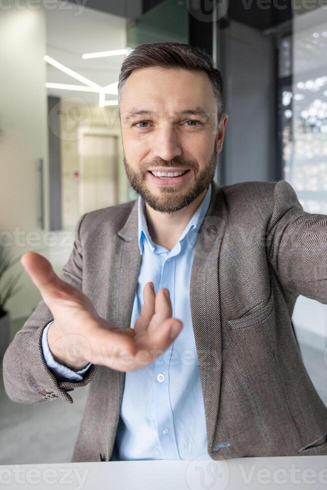 Confident businessman extending hand, engaging in an online call in a contemporary office setting. Ideal for business, communication, and corporate themes. photo