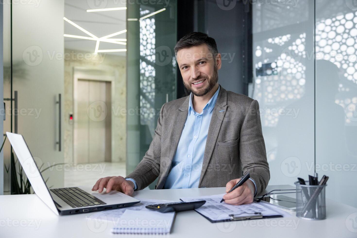 Confident businessman working in a modern office setting with laptop and documents, providing a sense of professionalism and productivity. photo