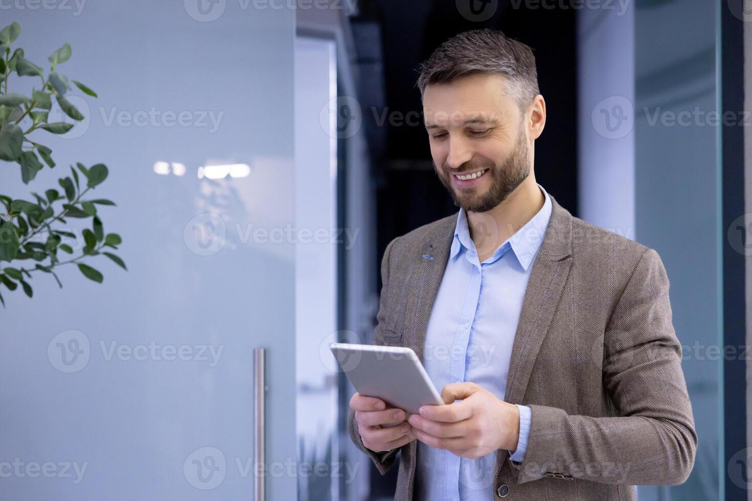 Mature experienced businessman inside office smiling contentedly, senior man holding tablet computer in hands, boss in business suit using analytical financial application. photo