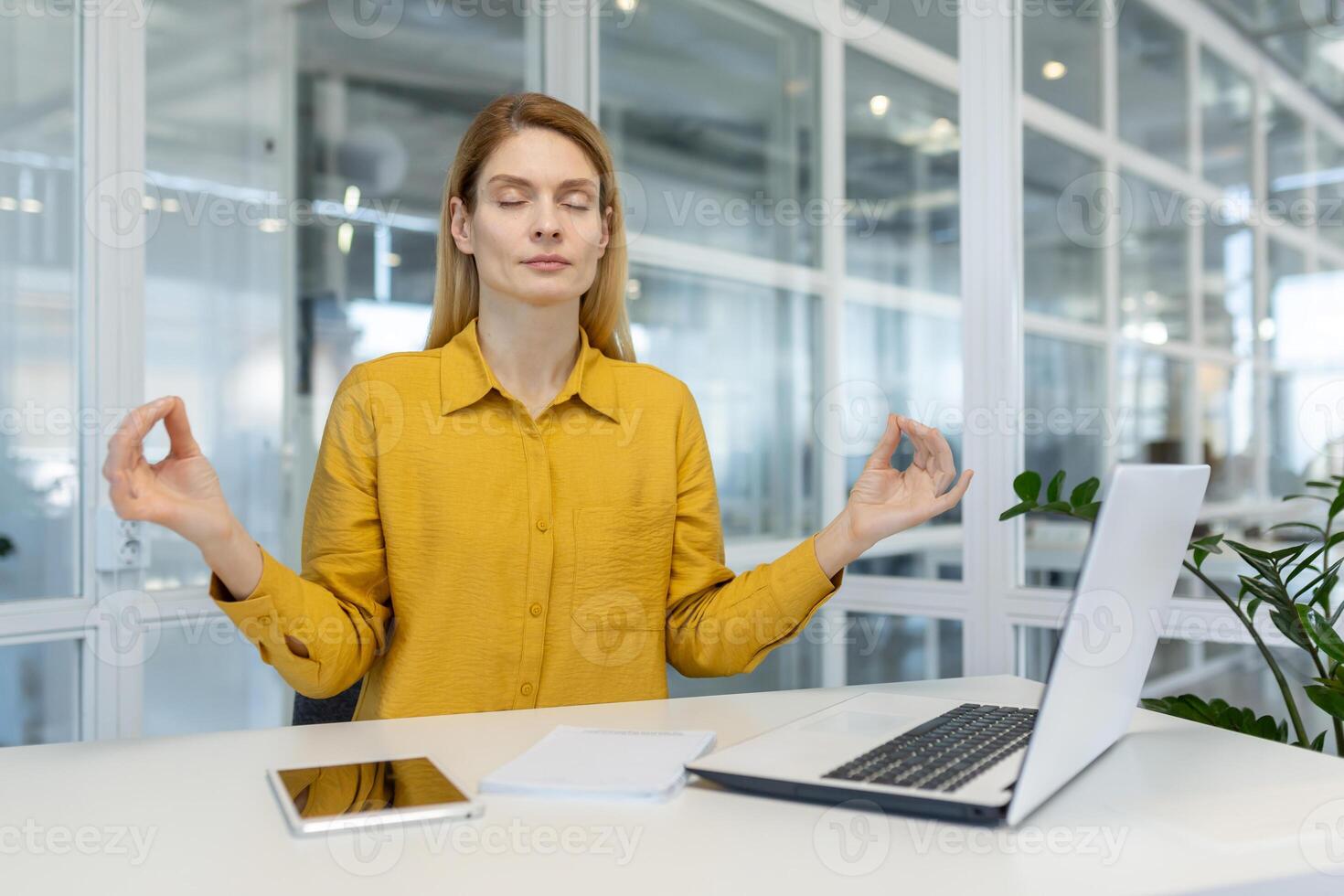 A businesswoman practices mindfulness meditation at her desk in a modern office, promoting workplace wellness and stress relief. photo