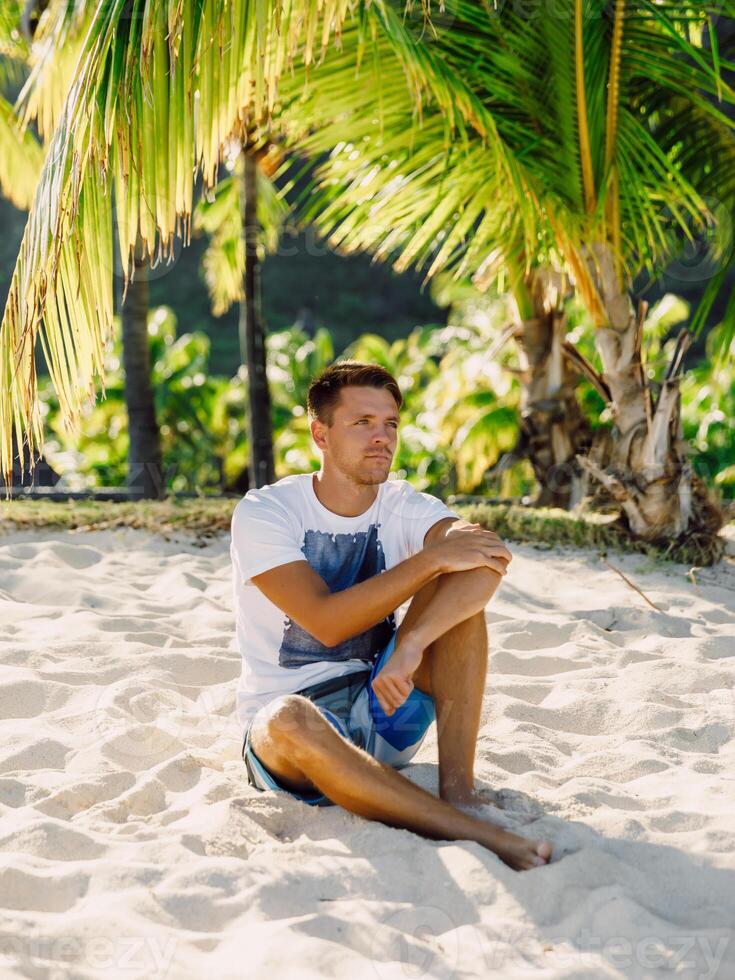 Handsome guy relaxing and sitting on beach. Slim man vacation on paradise beach photo