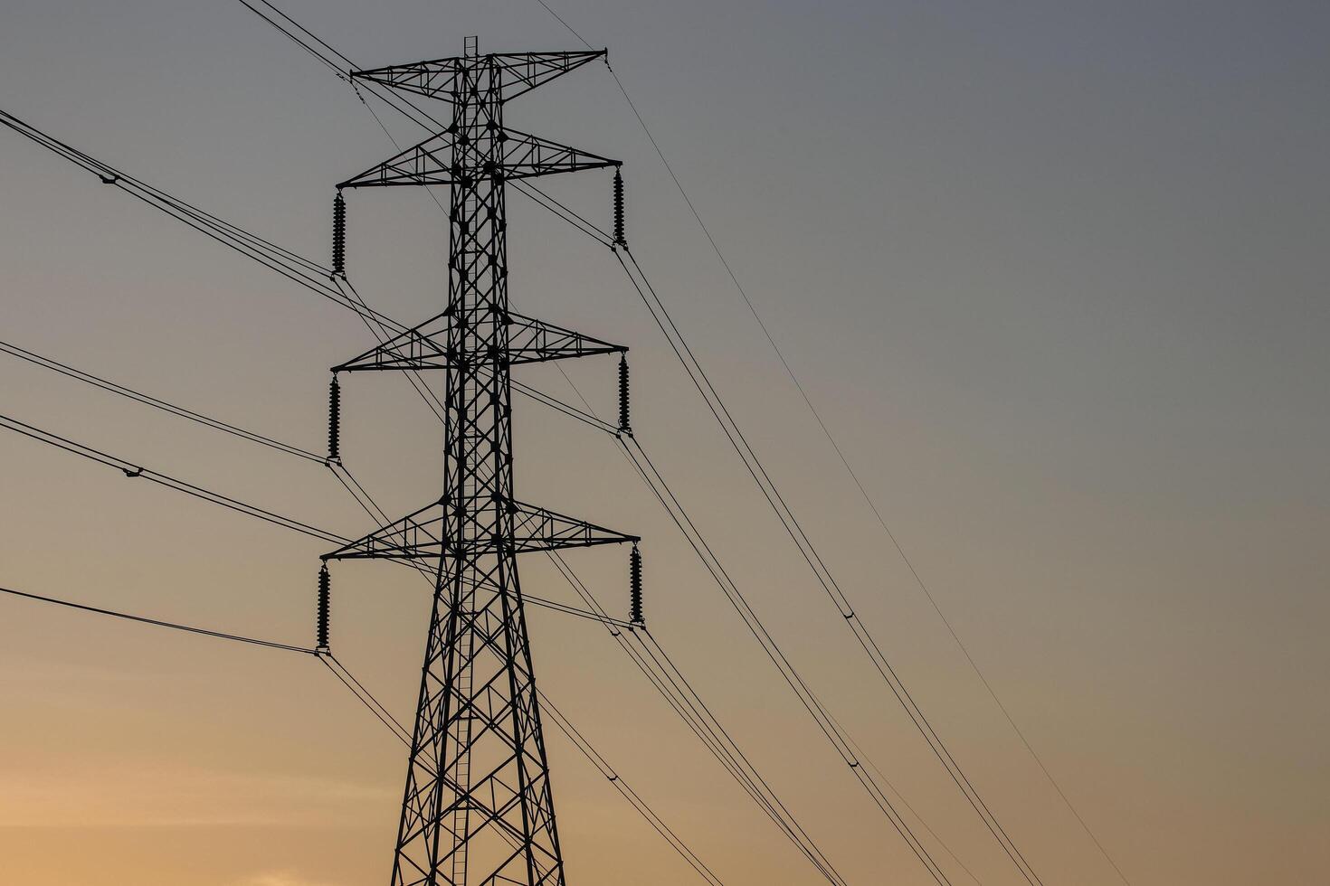 High voltage pole with many wires It was a silhouette with an orange sky as the background. photo