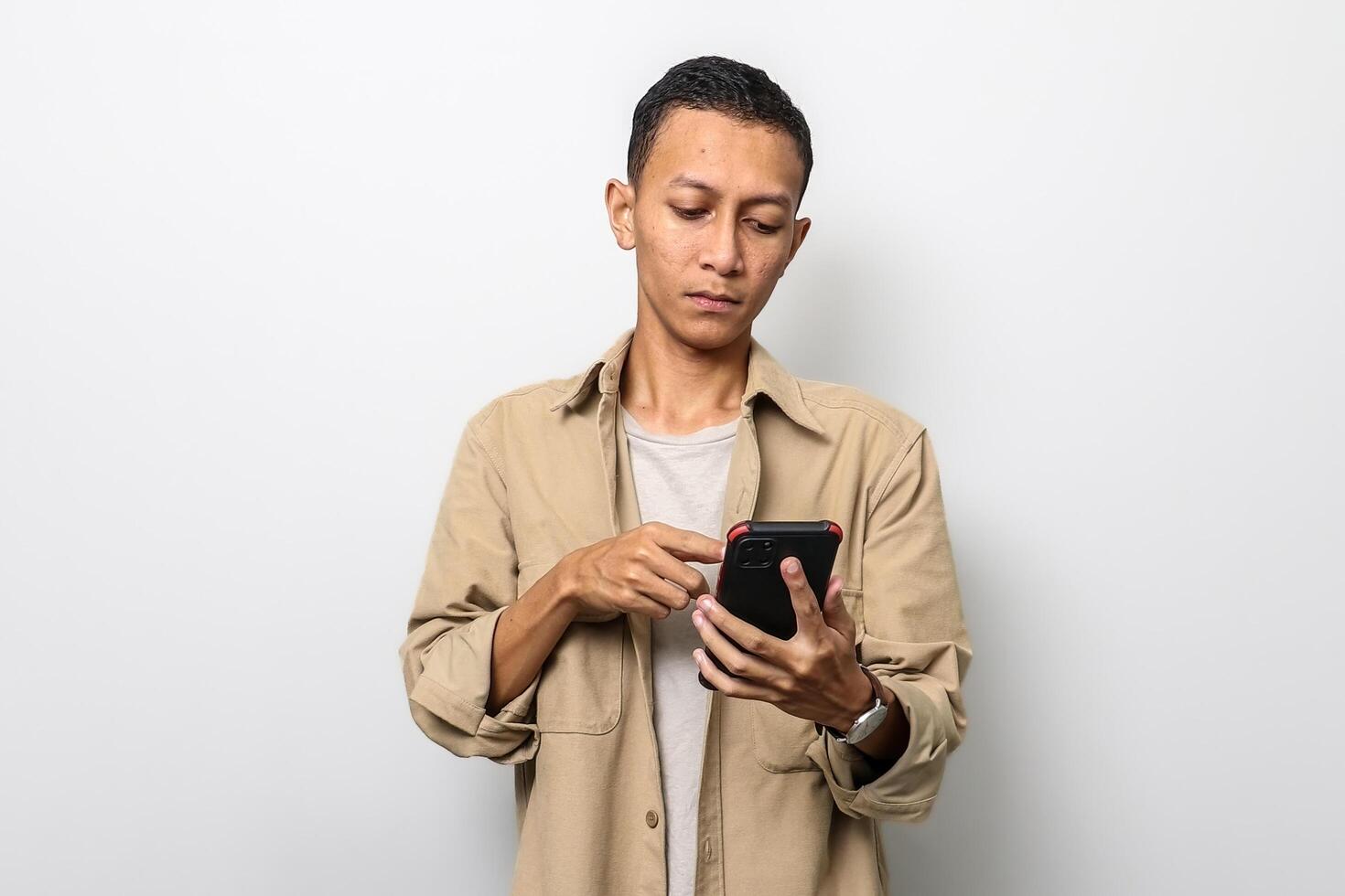 an asian business man with a tan jacket is touching a smartphone with a serious face photo