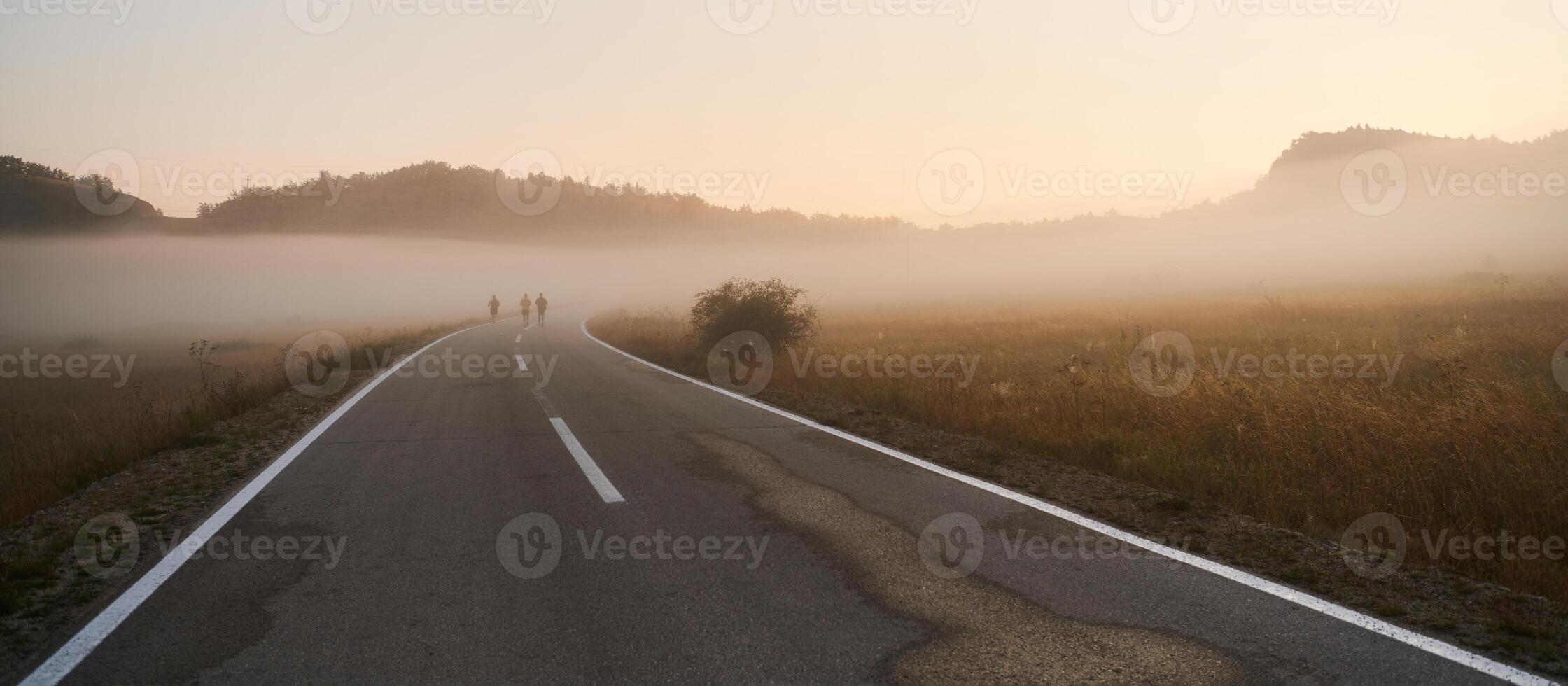 A group of friends, athletes, and joggers embrace the early morning hours as they run through the misty dawn, energized by the rising sun and surrounded by the tranquil beauty of nature photo