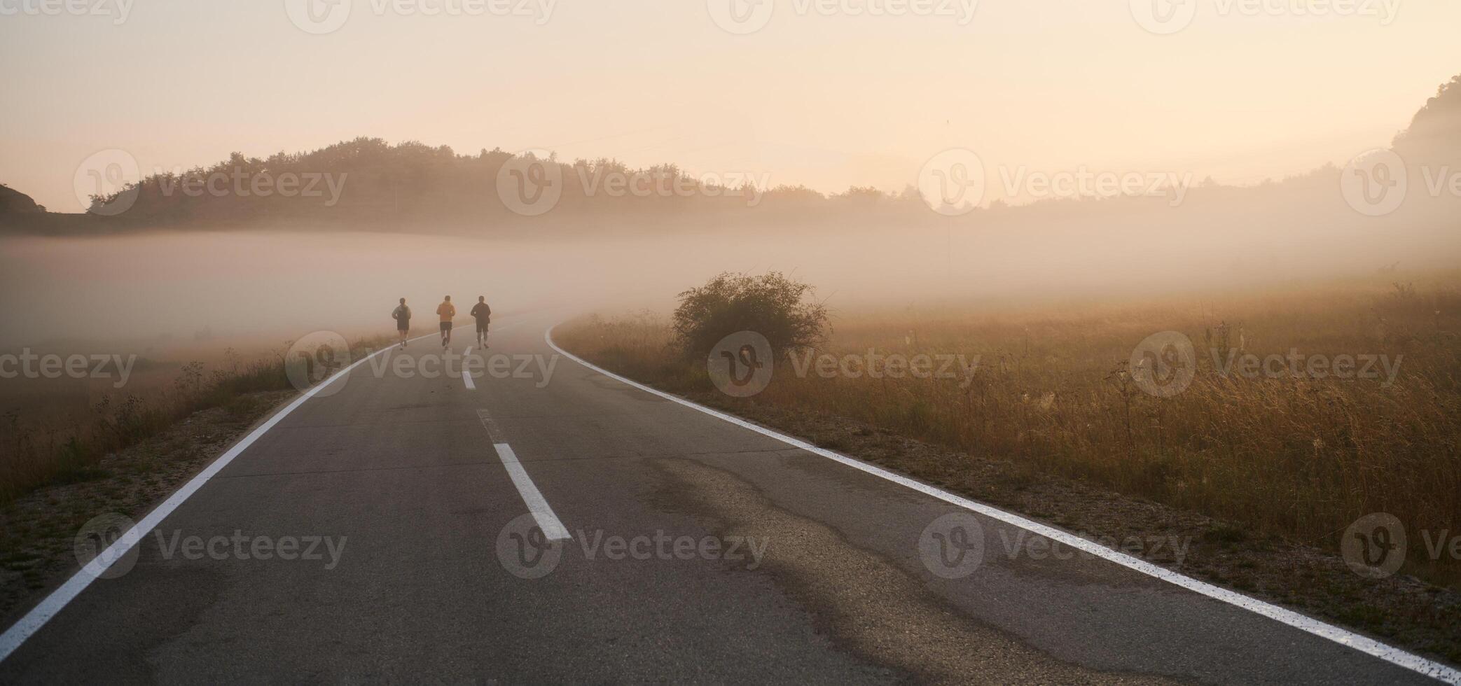 A group of friends, athletes, and joggers embrace the early morning hours as they run through the misty dawn, energized by the rising sun and surrounded by the tranquil beauty of nature photo