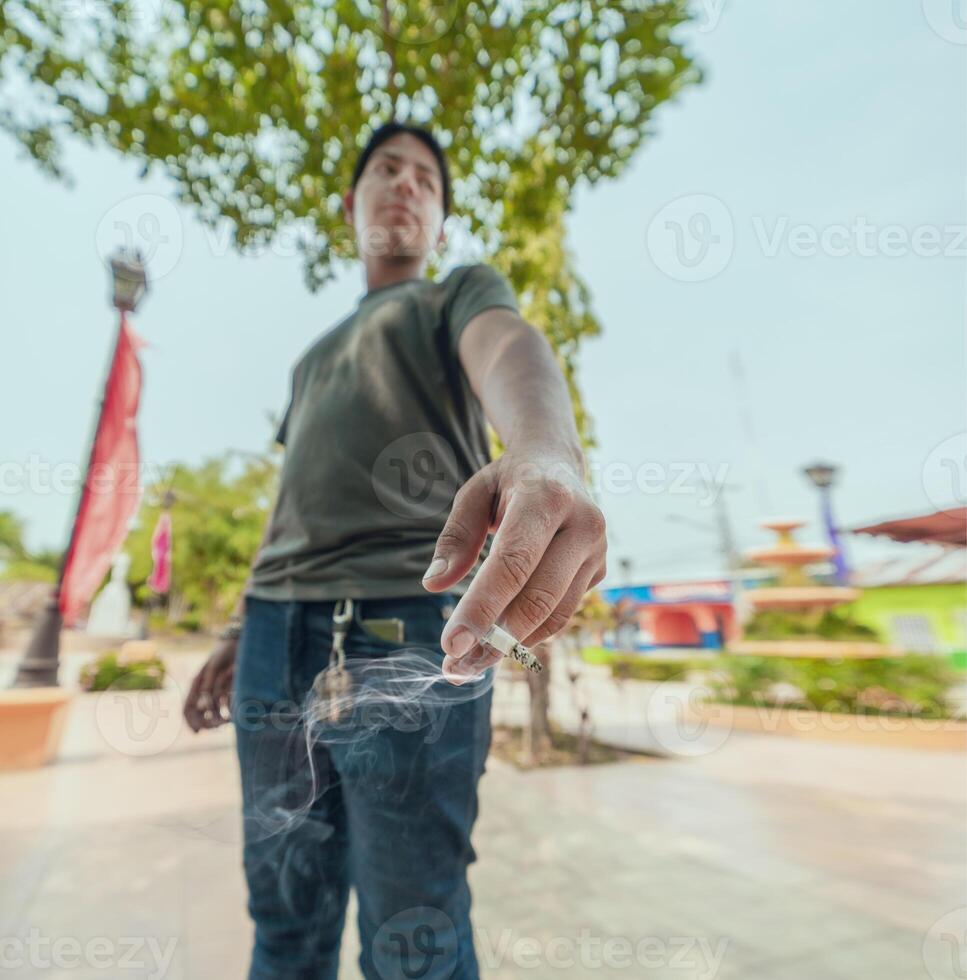Portrait of guy smoking on the street. Close-up of a young man showing a lit cigarette on the street photo