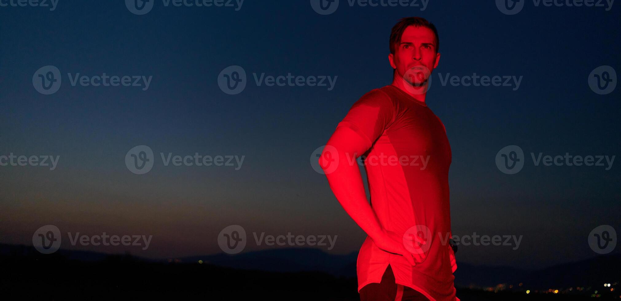 Athlete Strikes a Pose Under Red Nighttime Glow After Intense Daylong Marathon. photo