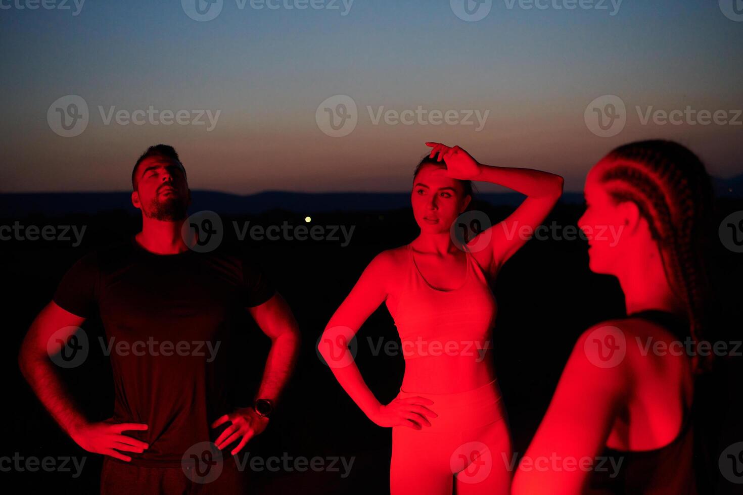 Diverse Athletes Unwind. Post-Marathon Rest Under Red Nighttime Glow. photo