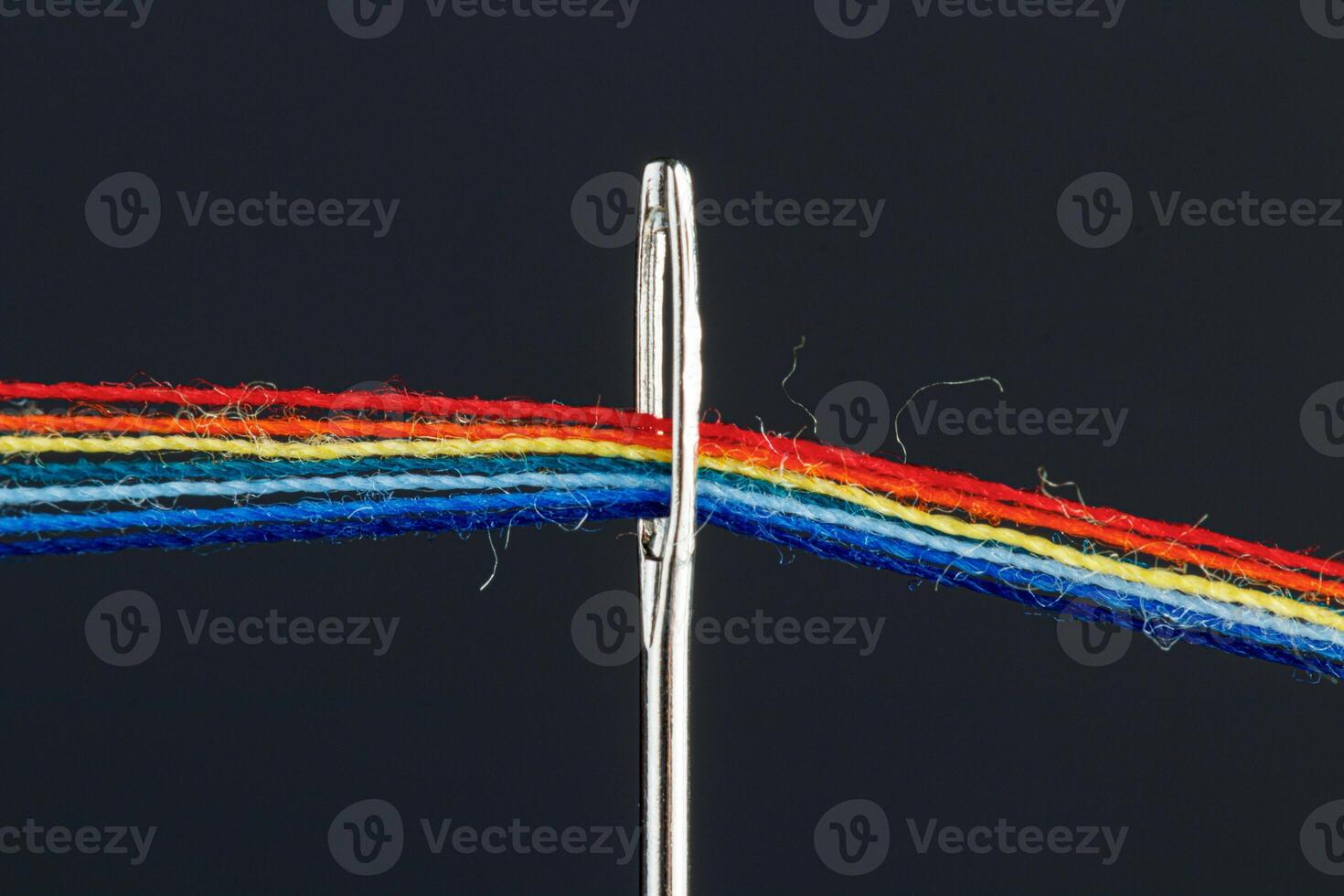 multi-colored threads for sewing in the form of a rainbow pass through an antique needle on a black background photo