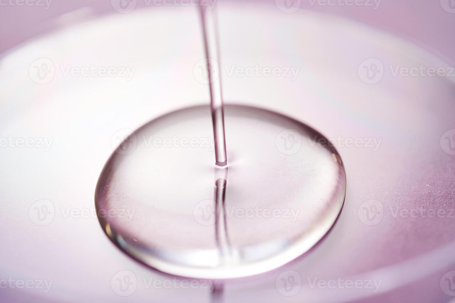 Serum or cosmetic oil flows into a transparent bowl on a purple background. photo