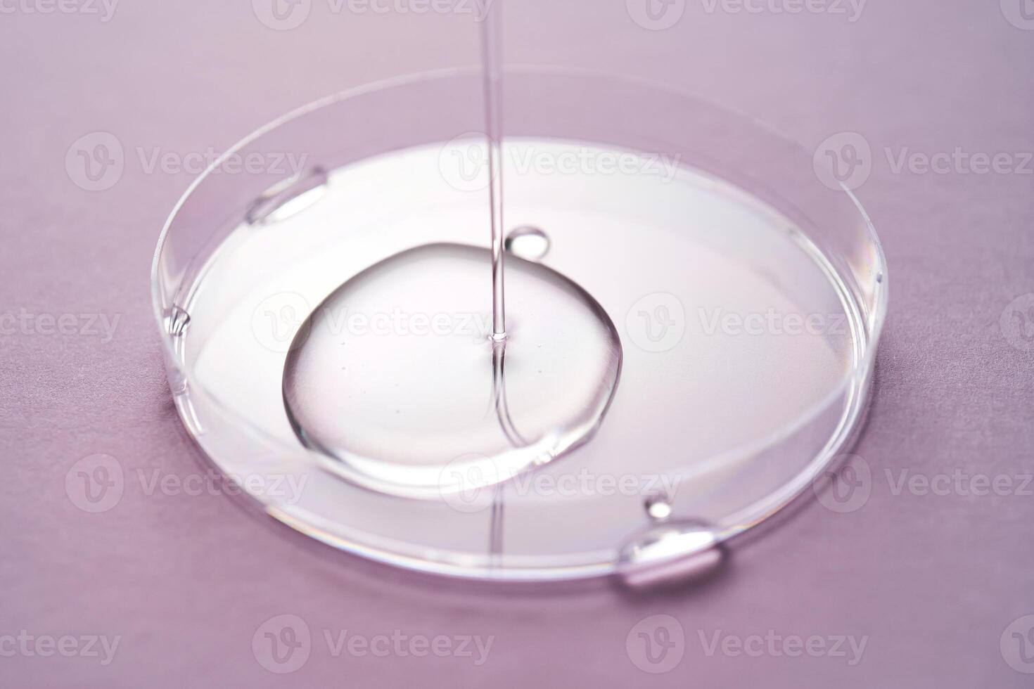 Serum or cosmetic oil flows into a transparent bowl on a purple background. photo