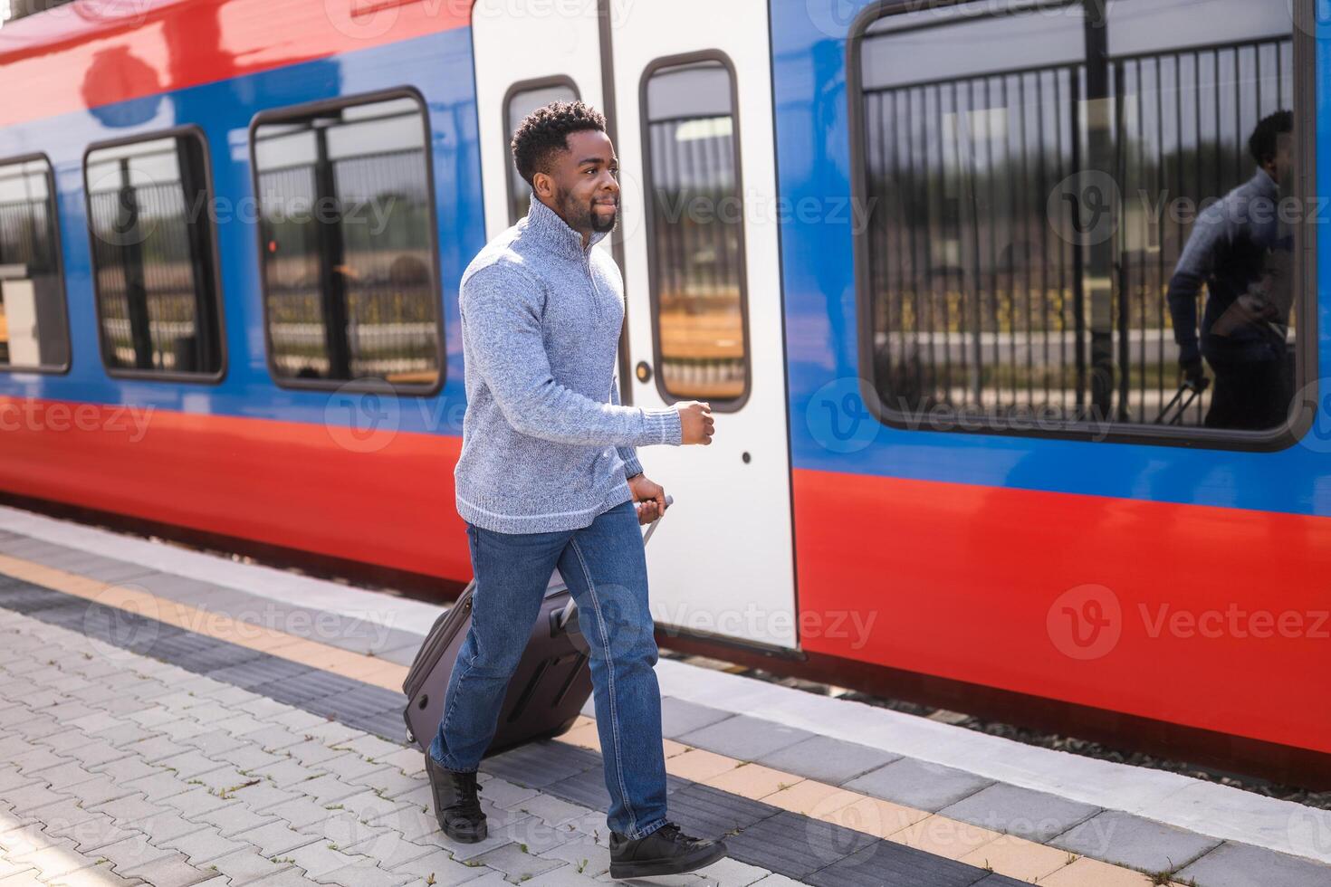 Man running to a leaving train along railway station with suitcase. photo