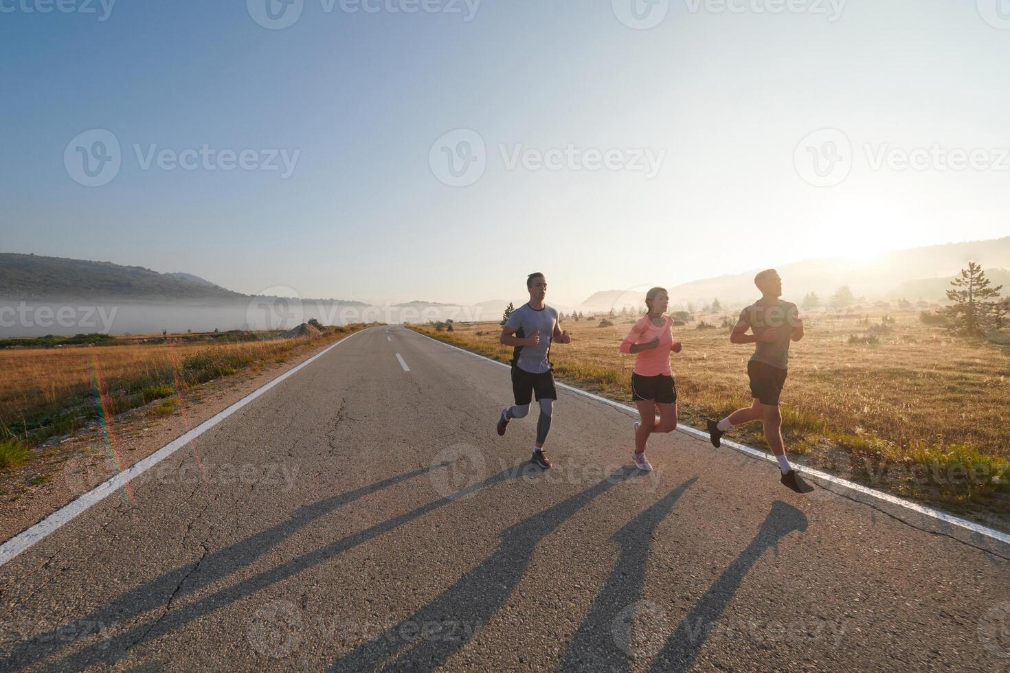 A group of friends, athletes, and joggers embrace the early morning hours as they run through the misty dawn, energized by the rising sun and surrounded by the tranquil beauty of nature photo