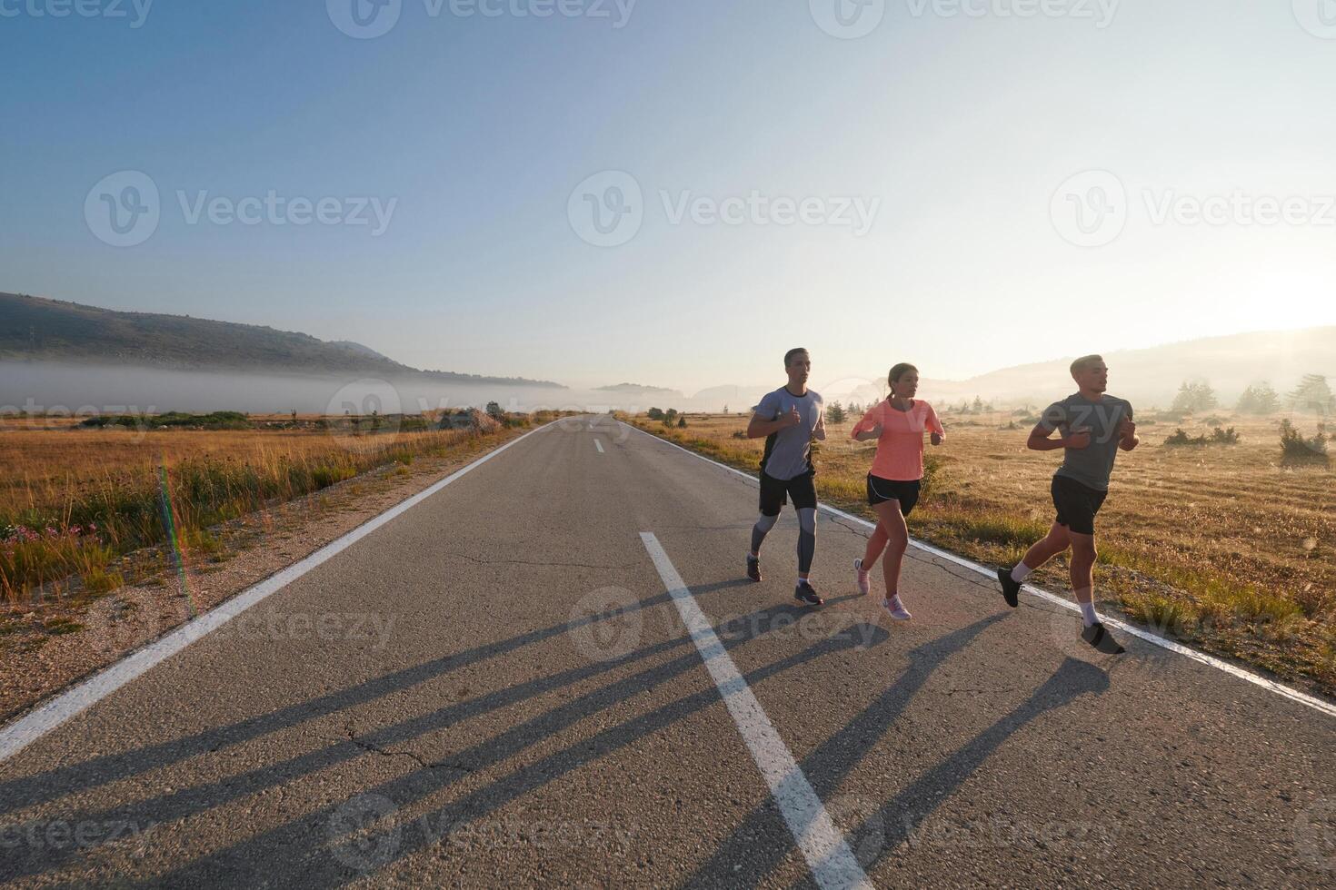A group of friends, athletes, and joggers embrace the early morning hours as they run through the misty dawn, energized by the rising sun and surrounded by the tranquil beauty of nature photo