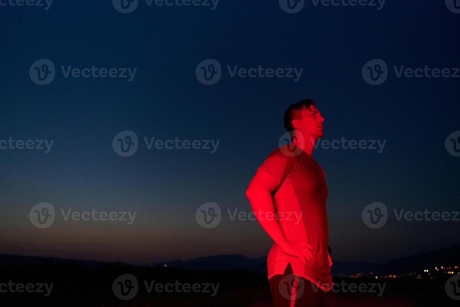 Athlete Strikes a Pose Under Red Nighttime Glow After Intense Daylong Marathon. photo