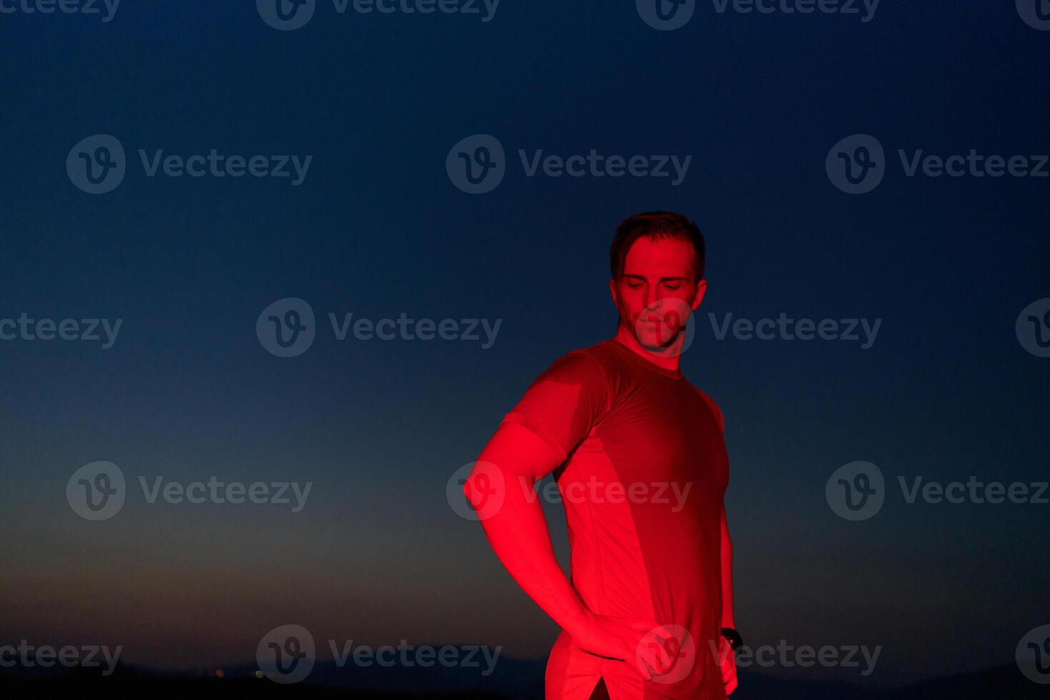 Athlete Strikes a Pose Under Red Nighttime Glow After Intense Daylong Marathon. photo