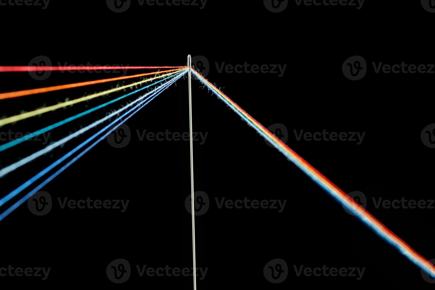 multi-colored threads for sewing in the form of a rainbow pass through an antique needle on a black background photo
