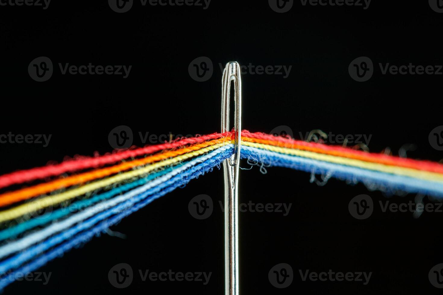 multi-colored threads for sewing in the form of a rainbow pass through an antique needle on a black background photo