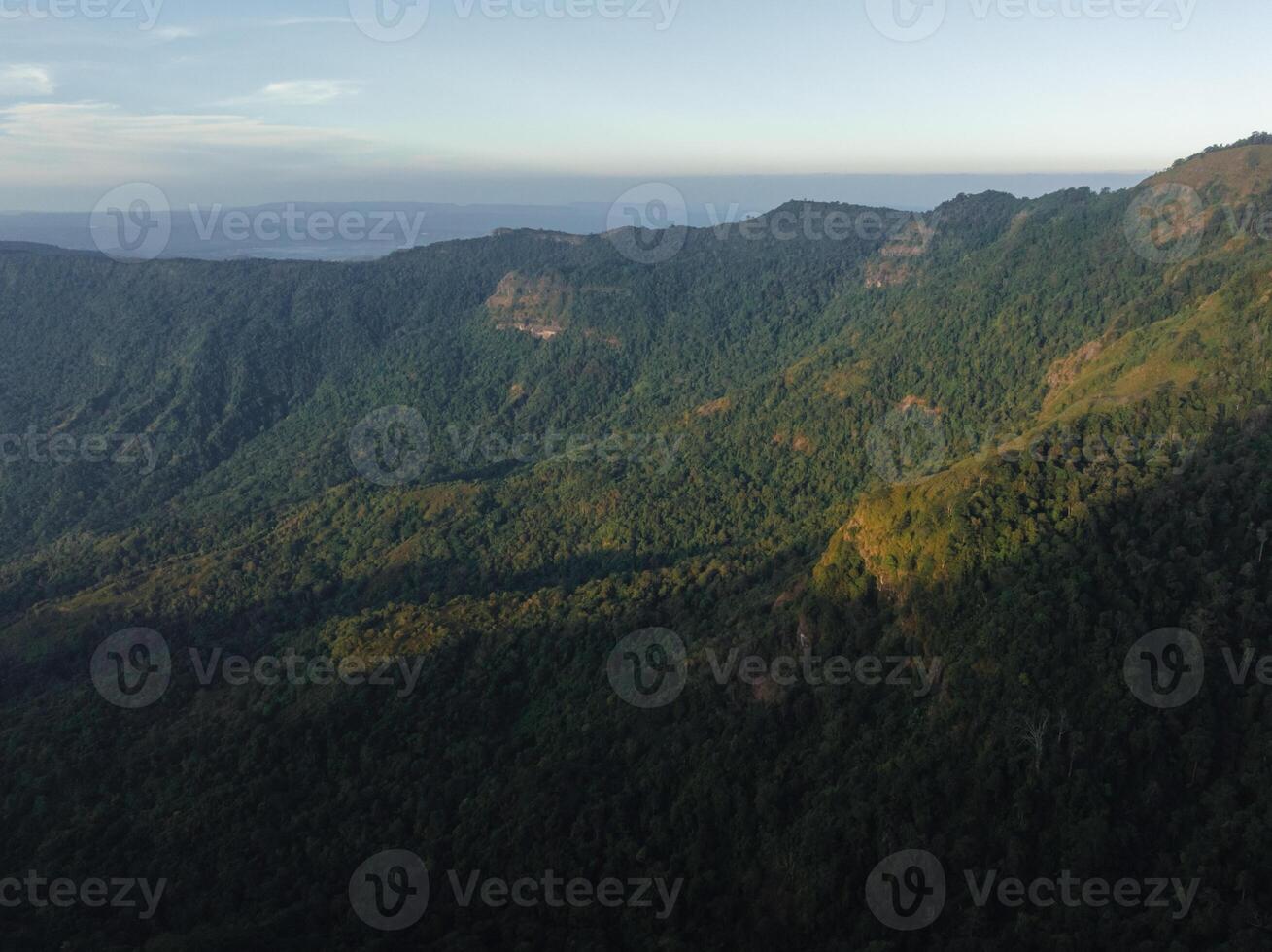 The fading light of dusk gently touches the slopes of a mountain blanketed with dense greenery, hinting at the vast wilderness photo