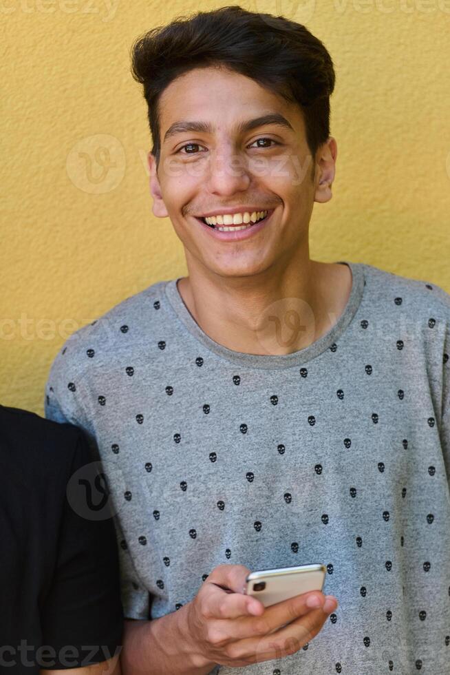 Middle Eastern Teenager Using Mobile Phone While Leaning Against Yellow Wall photo