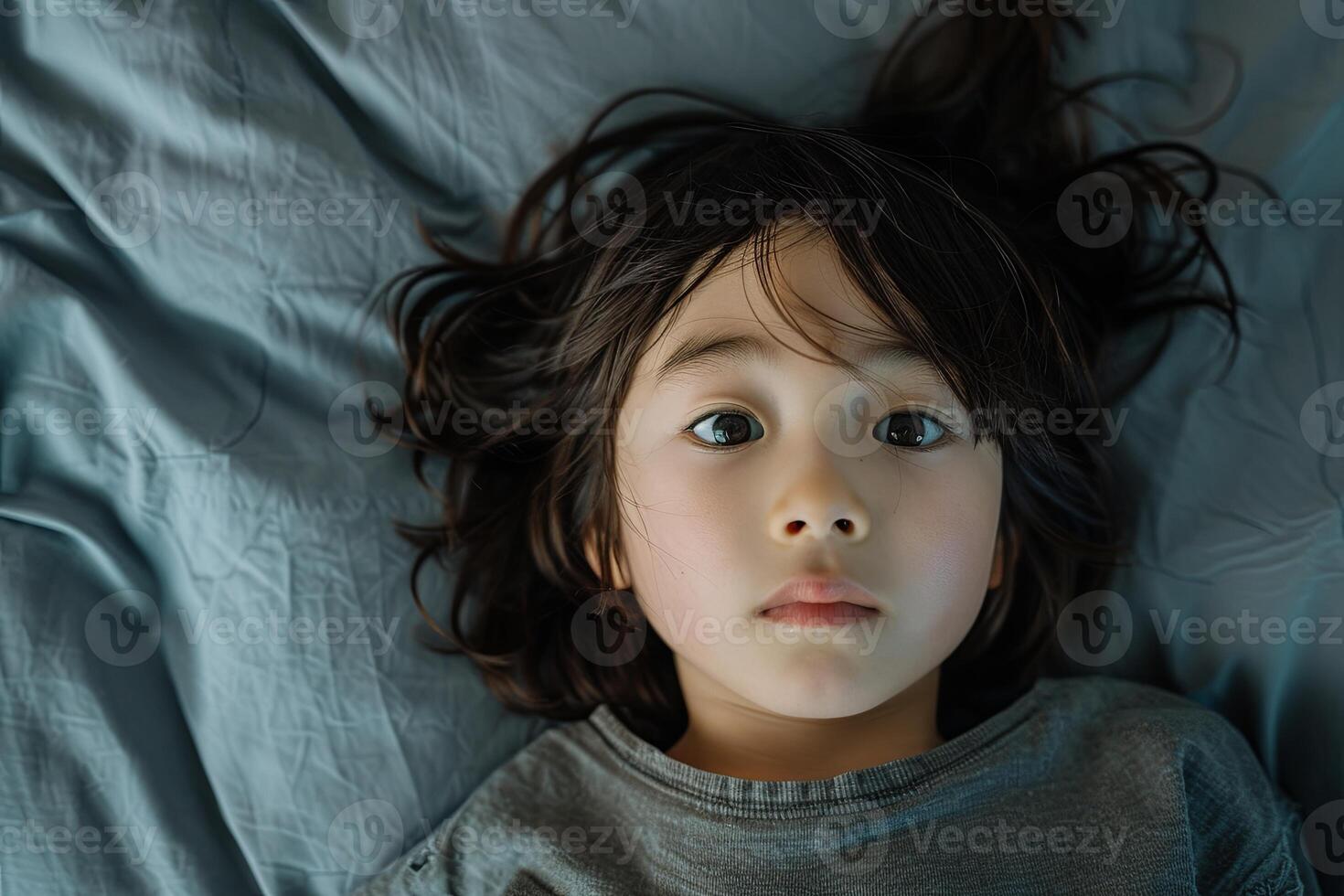Portrait of a 10 year old Japanese child lying on the bed, looking at the camera from directly above, with scared face and gloomy mood photo