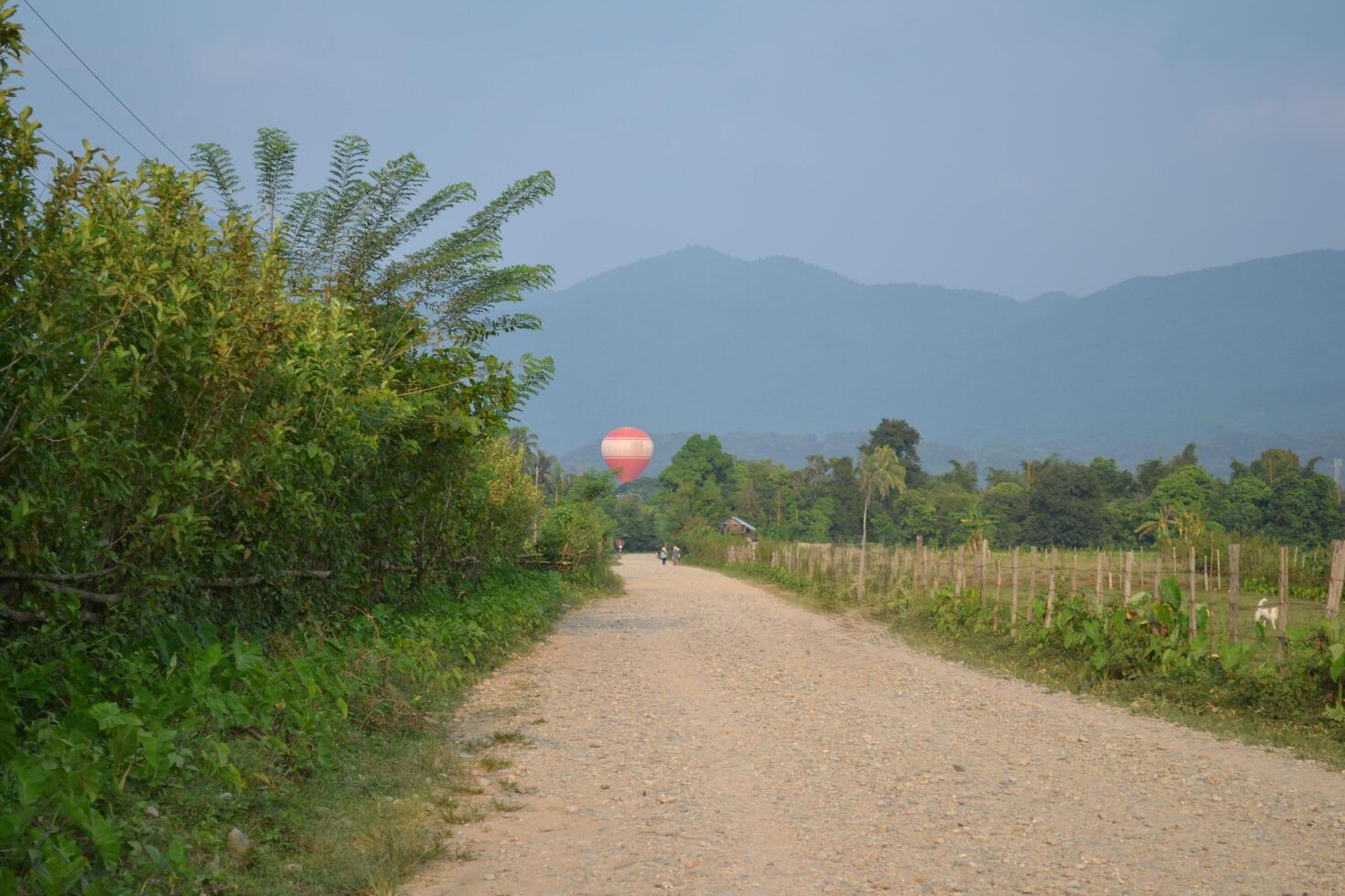 Hot air balloons pass high above the dusty dirt road photo