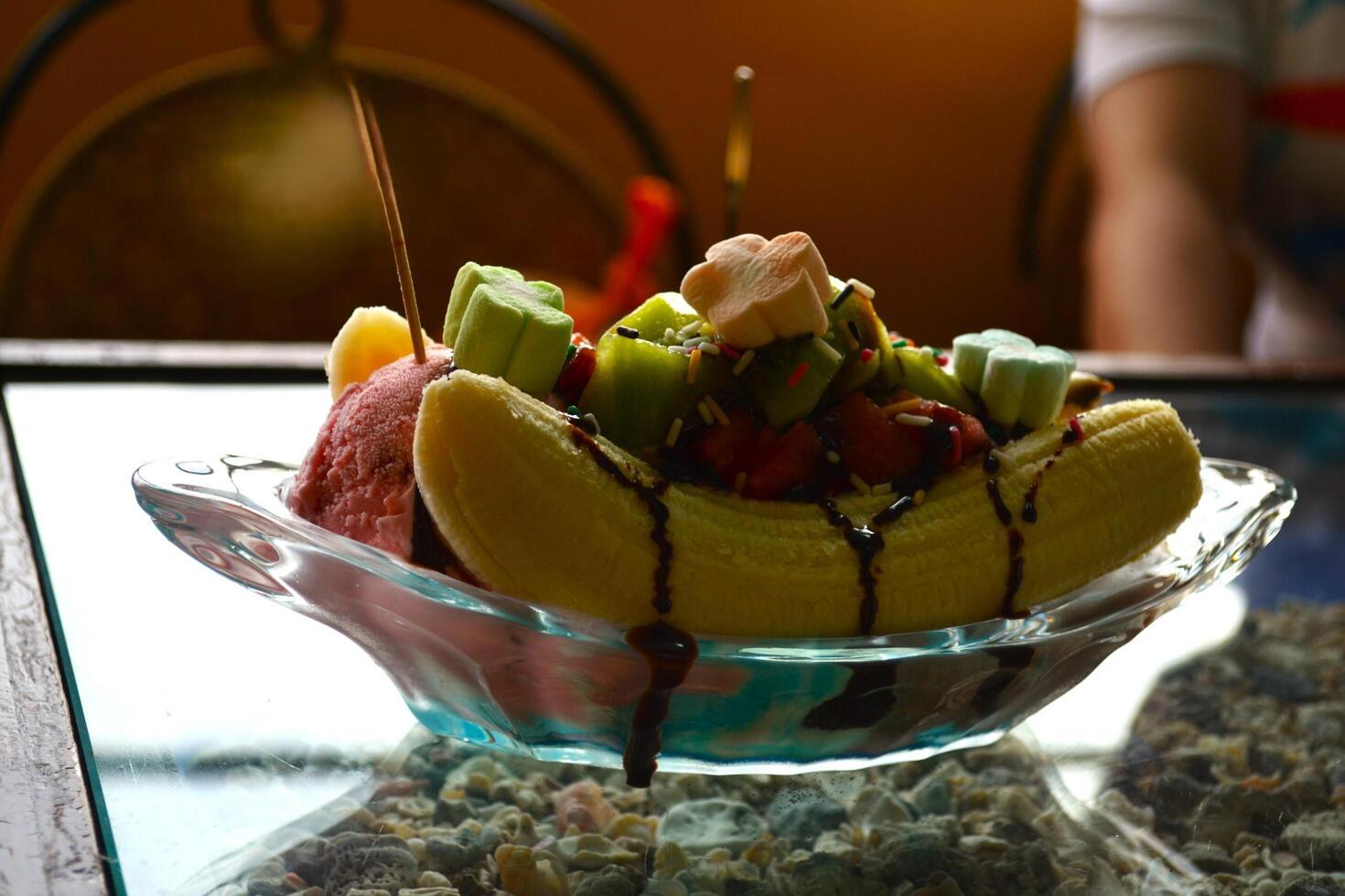A portion of iced banana split is served on a clear table photo