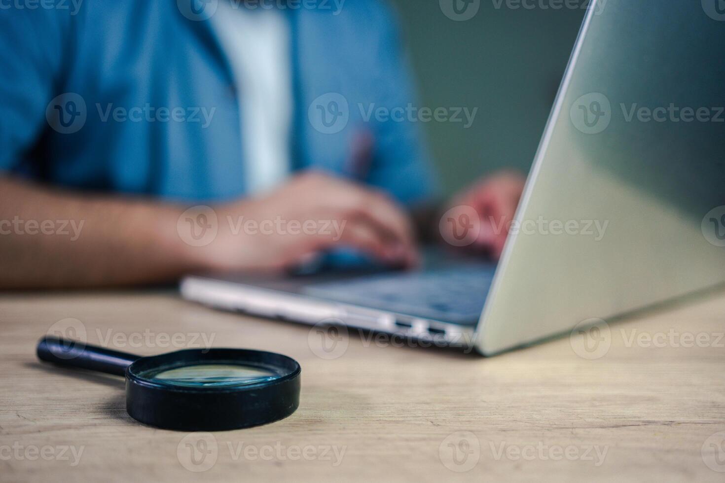 A businessman works on a computer with a magnifying glass on table. concept for analyzing data. Searching for information or evidence photo