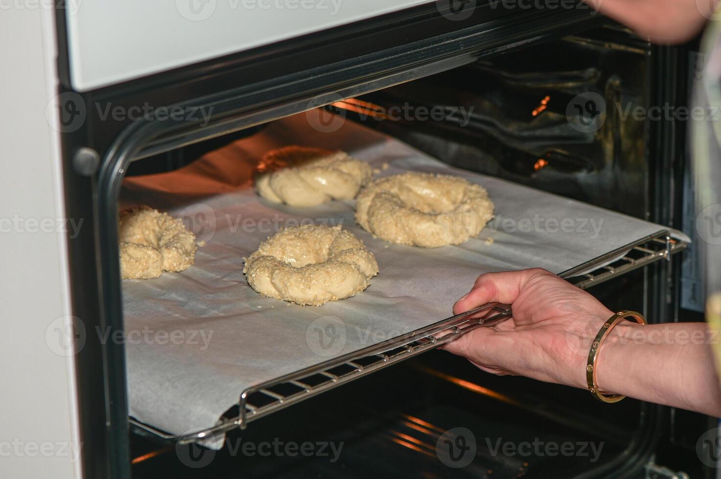 a woman puts a baking sheet with homemade sesame buns in the oven 3 photo