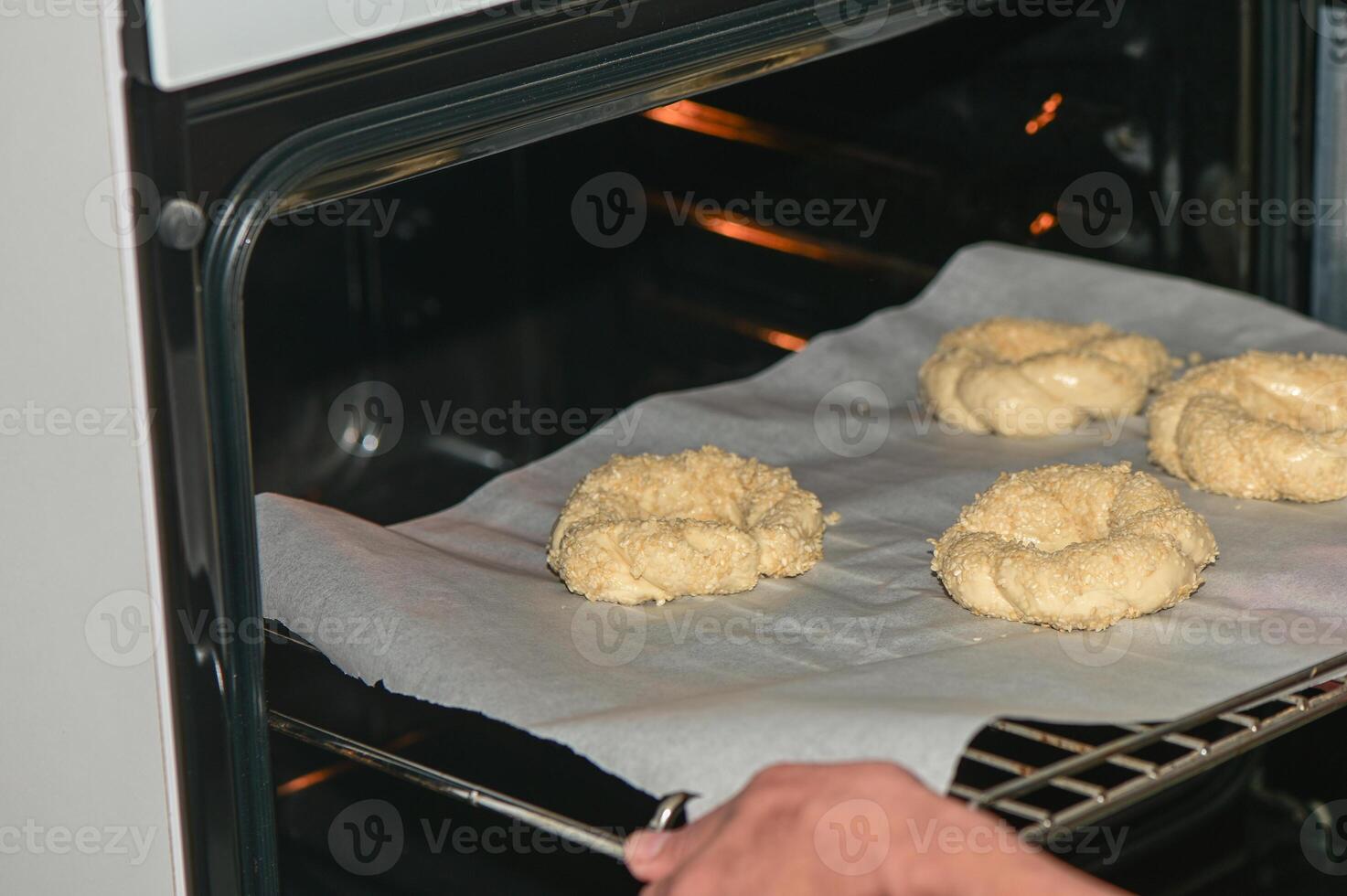 a woman puts a baking sheet with homemade sesame buns in the oven 2 photo