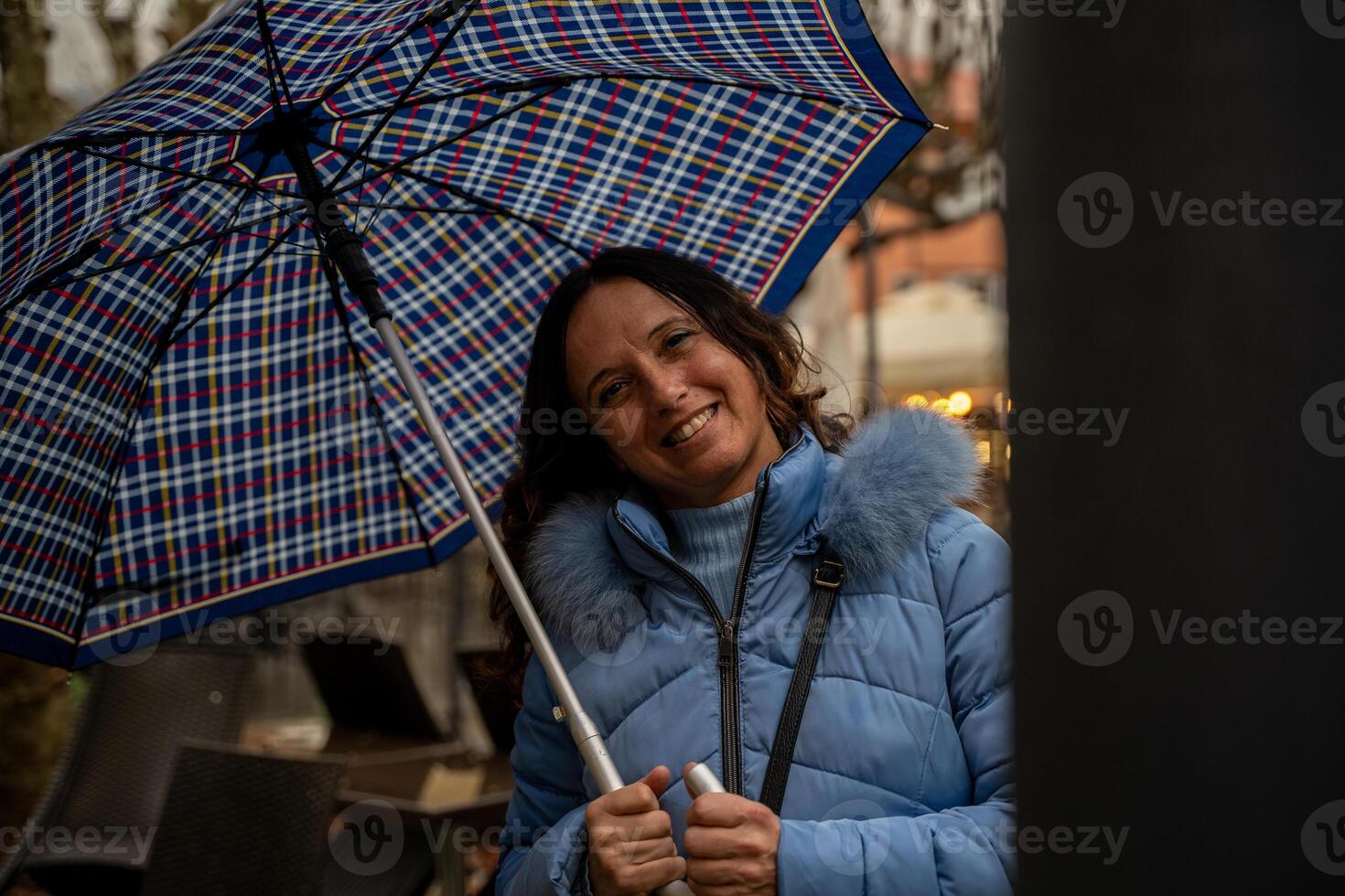 beautiful middle aged smiling woman walking in the rain with an umbrella in front of the tables of an cafe photo