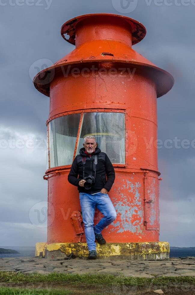 middle aged man photographer posing with camera in front of a red lighthouse photo