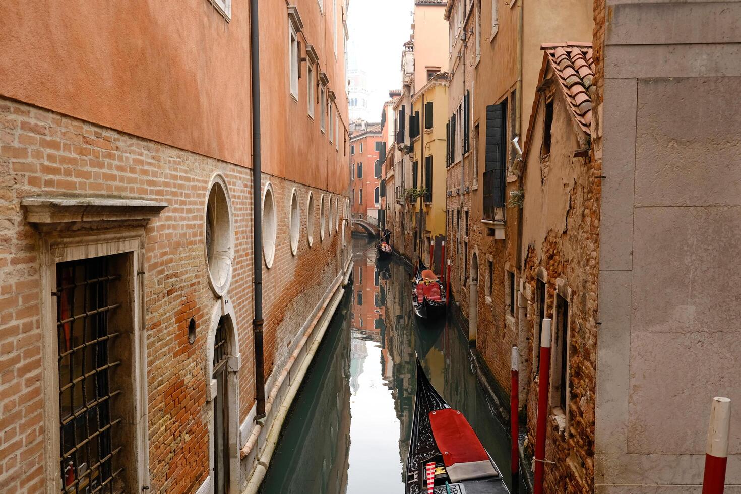 An empty gondola is parked in a Venetian canal. View of the bridge over the canal, reflection of the bridge in the water. Typical narrow street with historical houses in Venice. photo