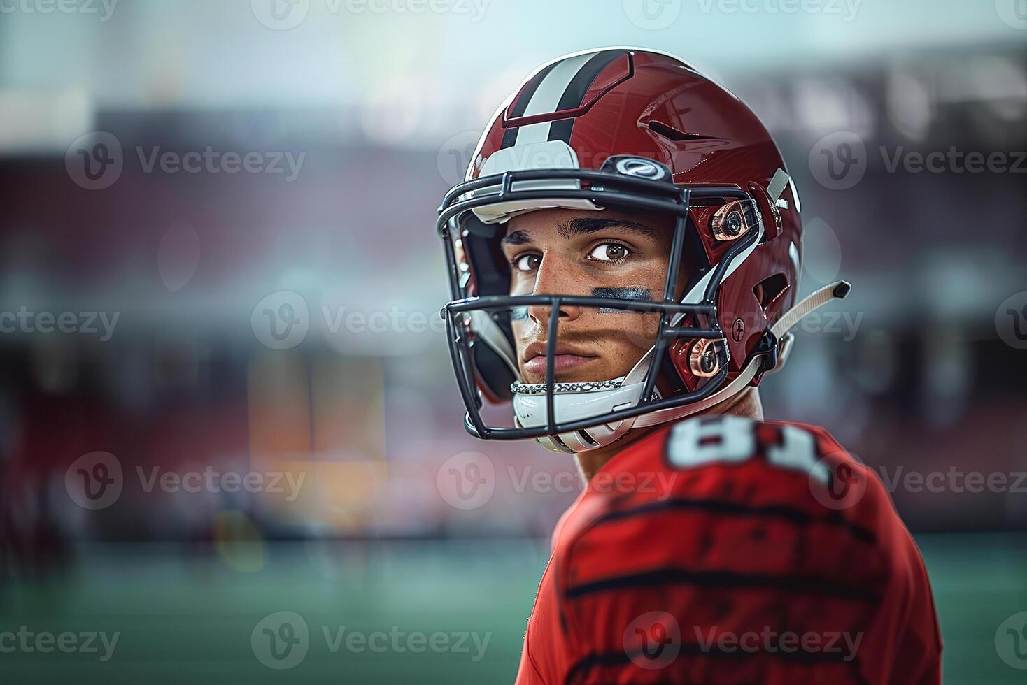 An American football player in a red helmet and uniform stands sideways, turning his head to the left. Copy space photo