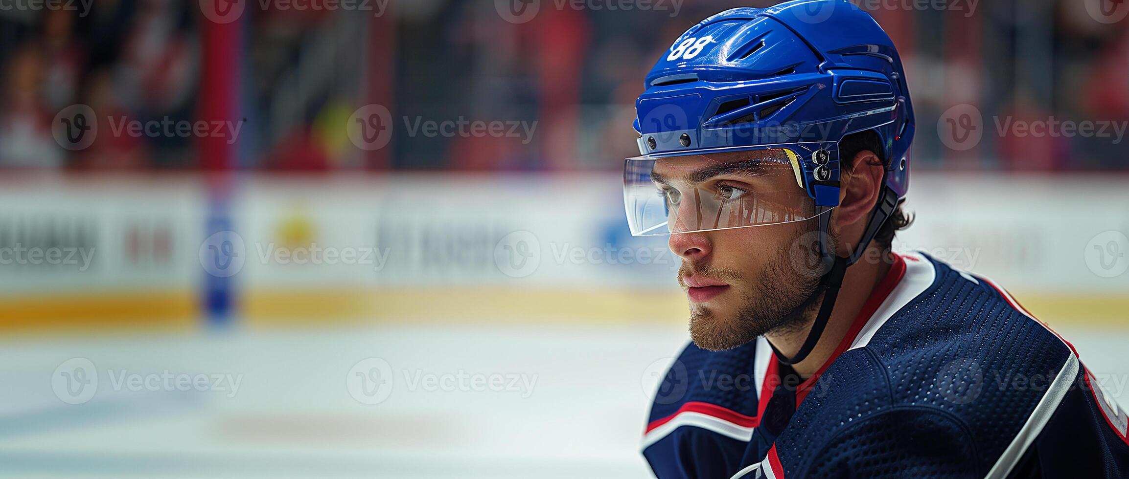 A hockey player in a blue helmet and jersey stands sideways. Hockey arena in the background. Copy space photo