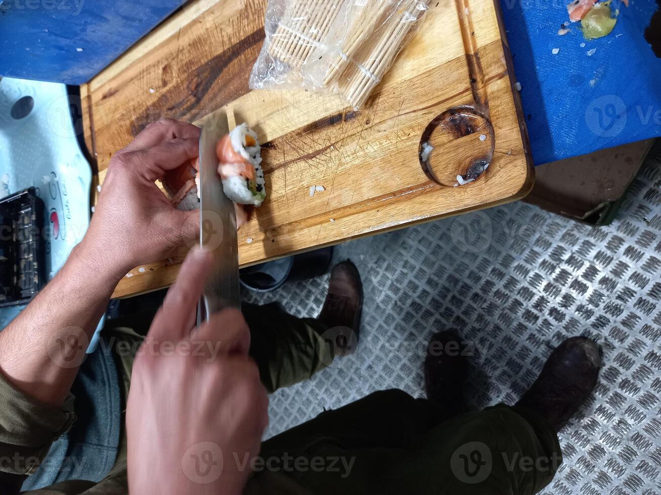 A man cuts the Sushi with a knife on a cutting board. photo