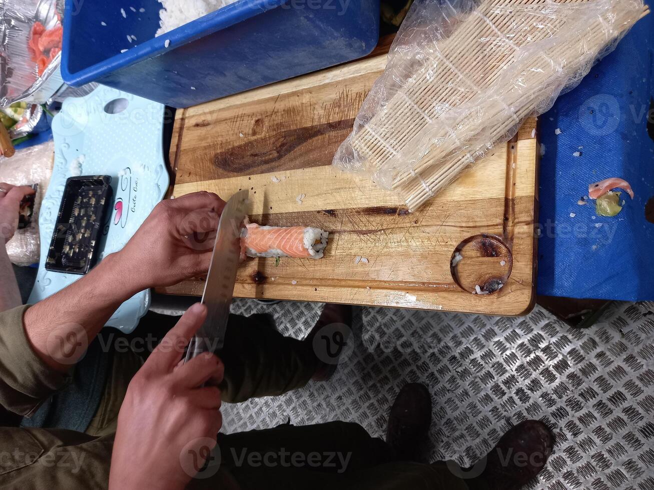 A man cuts the Sushi with a knife on a cutting board. photo
