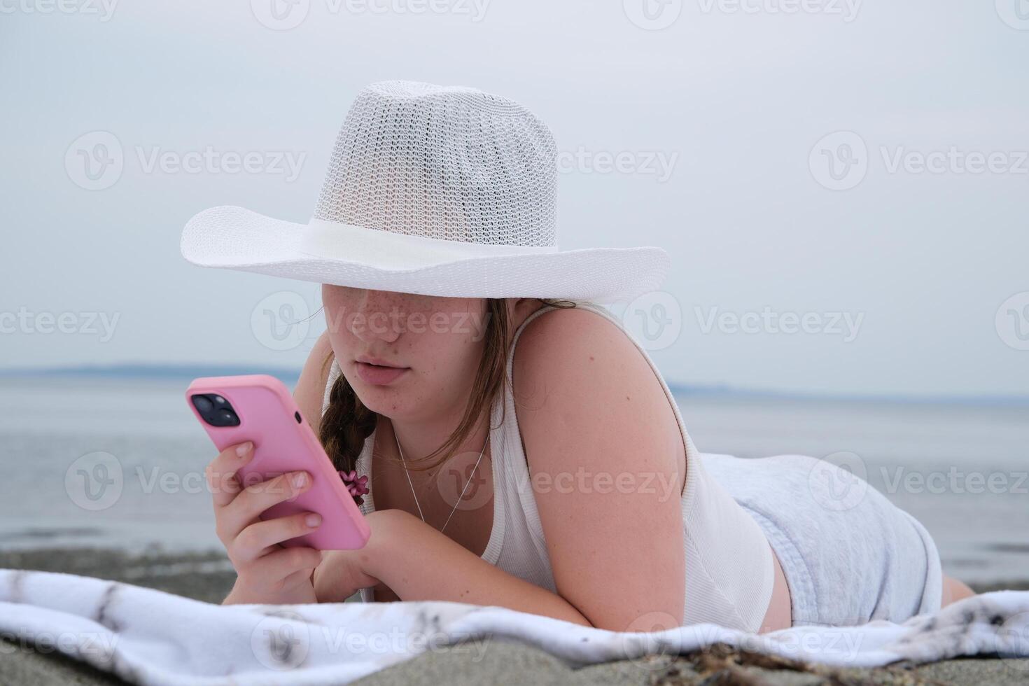 Girl using cellphone on a sea ocean shore. Young girl on the beach with your smartphone. photo