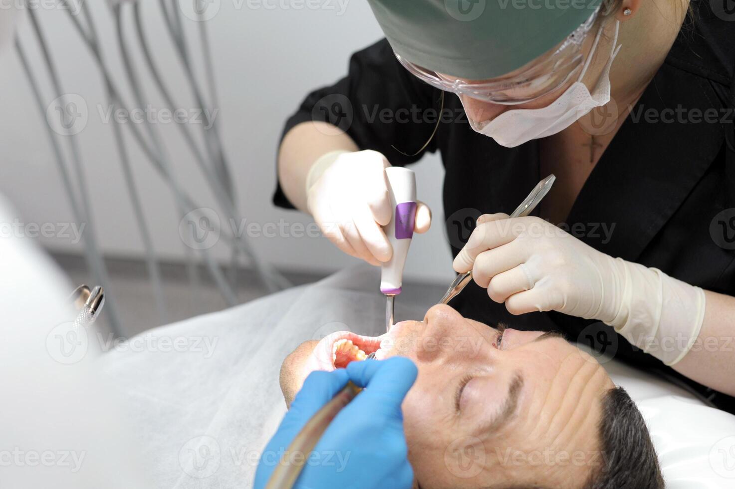 woman doctor dentist removes man patient tooth heavy easy extraction hard tooth extraction, tooth extraction tools Gracie curette, piezo scaler, piezo scaler attachment, piezo scaler wrench, luxator, photo