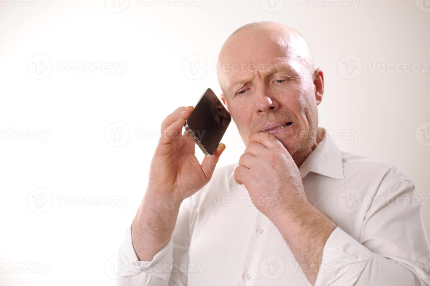 Senior man feeling upset having phone conversation depressed by hearing bad news adult man in white shirt grabbed his head and is upset, he listens to the news from the phone, he is talking to someone photo