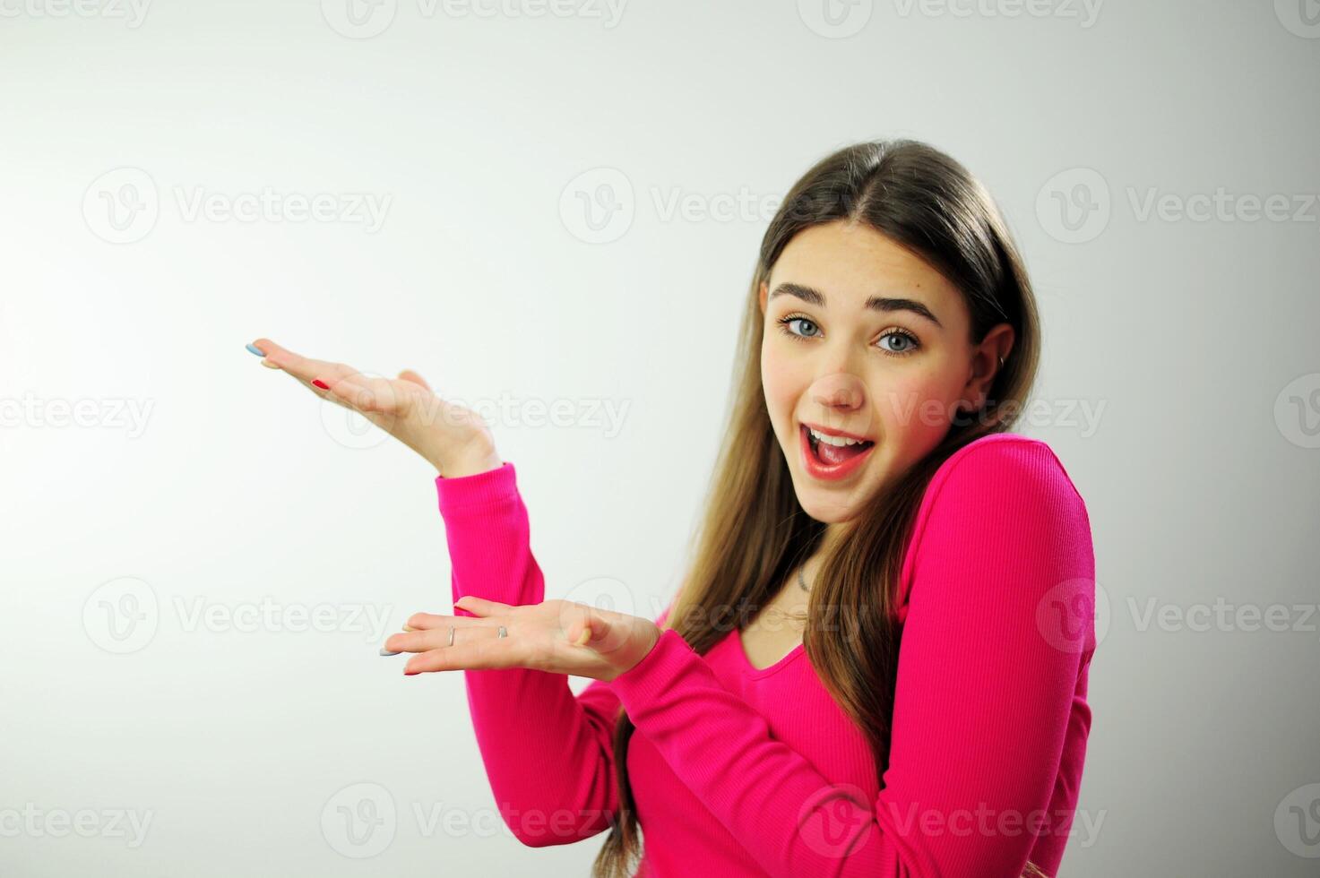 Thoughtful woman Show hands on empty space advertising looks pensively above dressed in casual pink jumper poses against blank copy space for your advertising content thinks about future photo