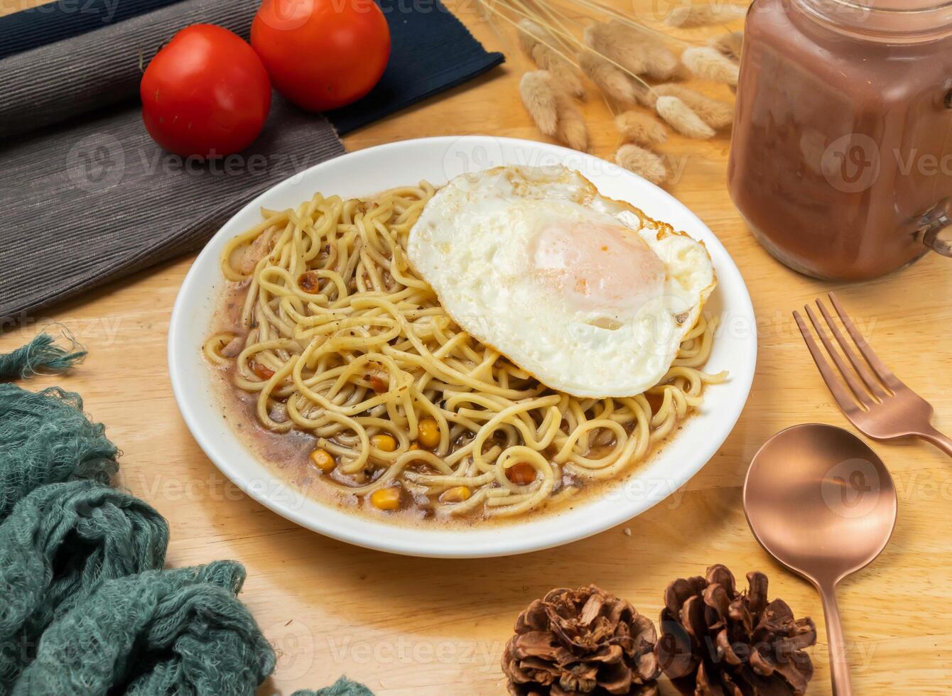 Black pepper egg teppanyaki noodles with cherry tomato, spoon and fork served in dish isolated on wooden table side view of taiwan food photo