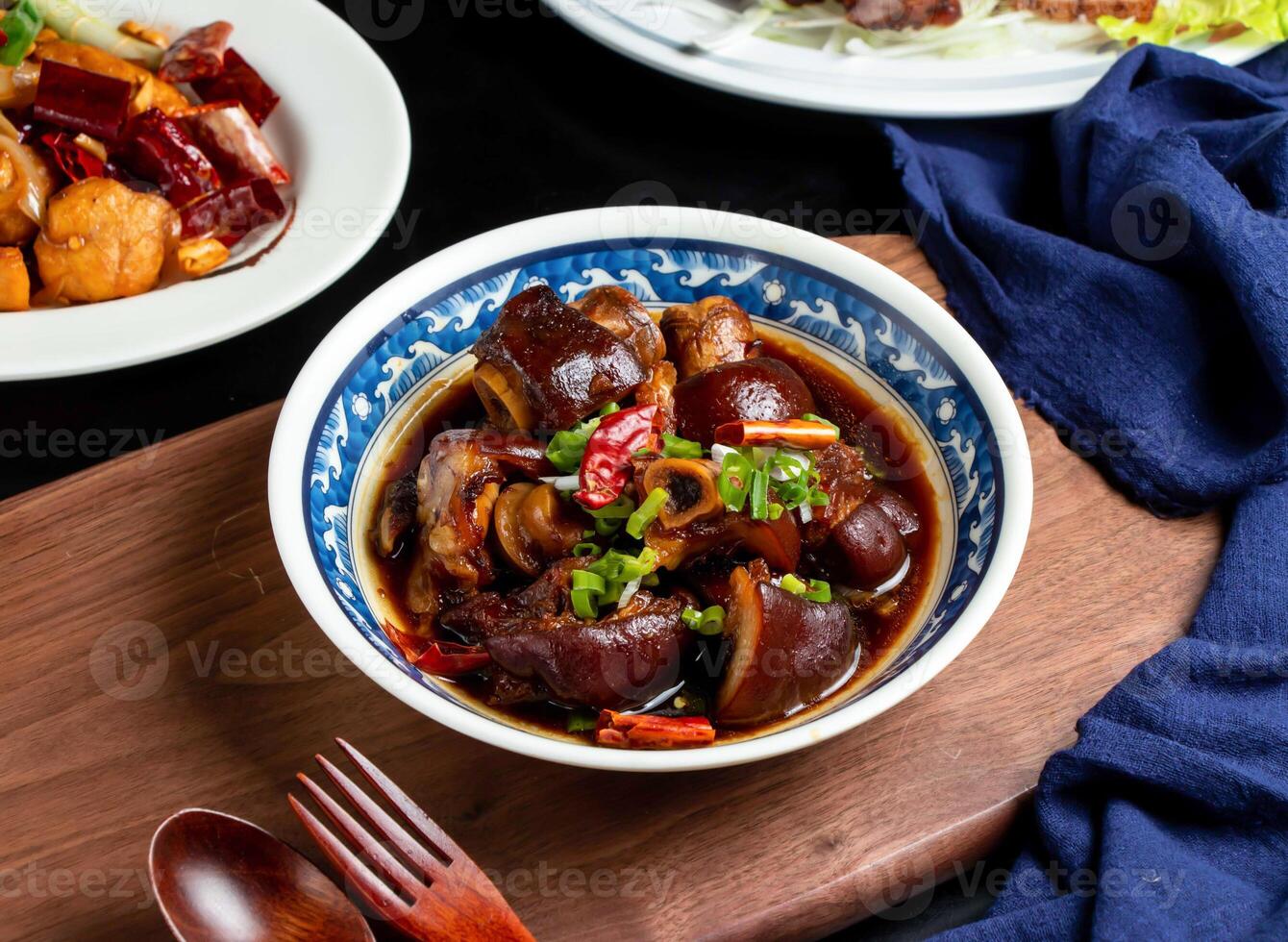 Braised pig feet with spring onion, red pepper, spoon and fork served in dish isolated on wooden board side view of taiwan food photo